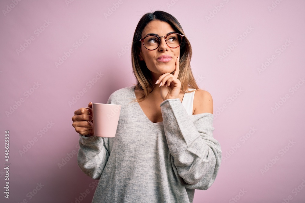 Young beautiful brunette woman wearing glasses drinking pink mug of coffee serious face thinking about question, very confused idea Young beautiful brunette woman wearing glasses drinking pink mug of coffee serious face thinking about question, very confused idea
