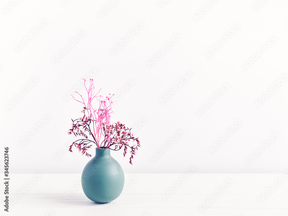 Flower composition. A bouquet of dried plants (flowers or leaves) is in a small green vase on a white wooden table. Behind is a white wall. Copy space. Flower composition. A bouquet of dried plants (flowers or leaves) is in a small green vase on a white wooden table. Behind is a white wall. Copy space.
