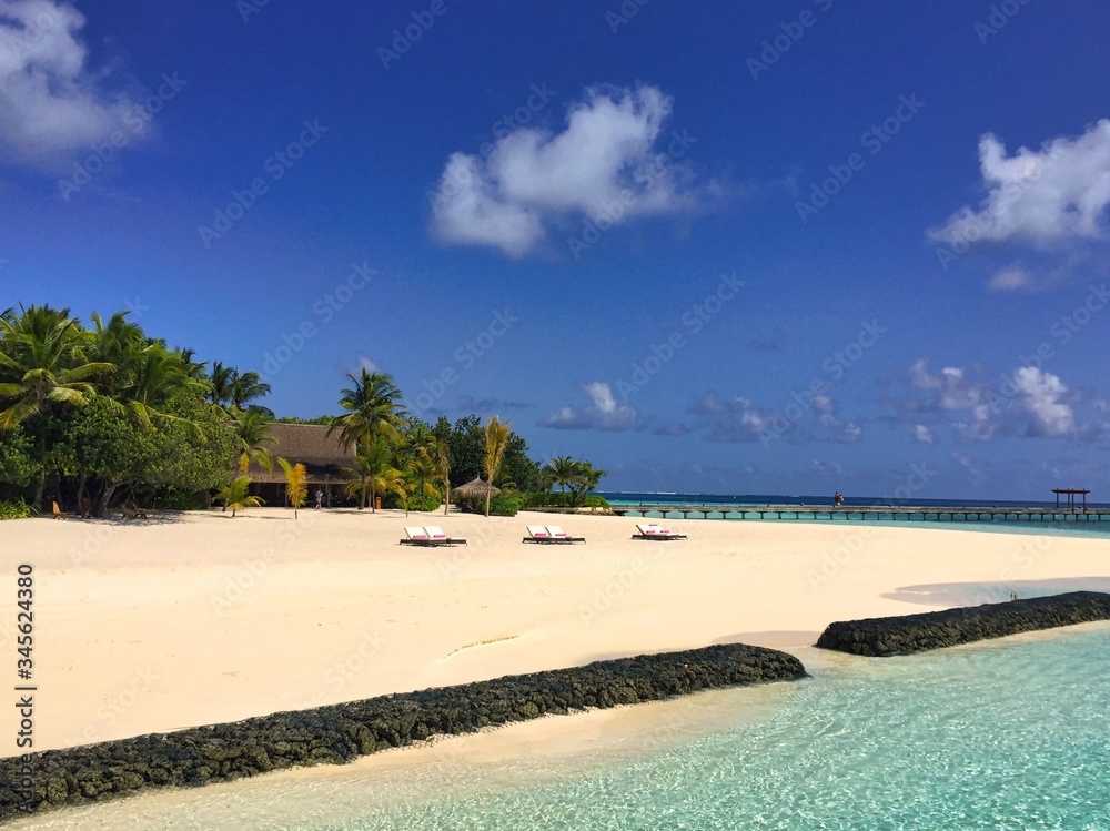 A picture of a Maldivian shore at Constance Moofushi Maldives with clear blue Laccadive sea, beautiful sand, palms and blue sky at the background