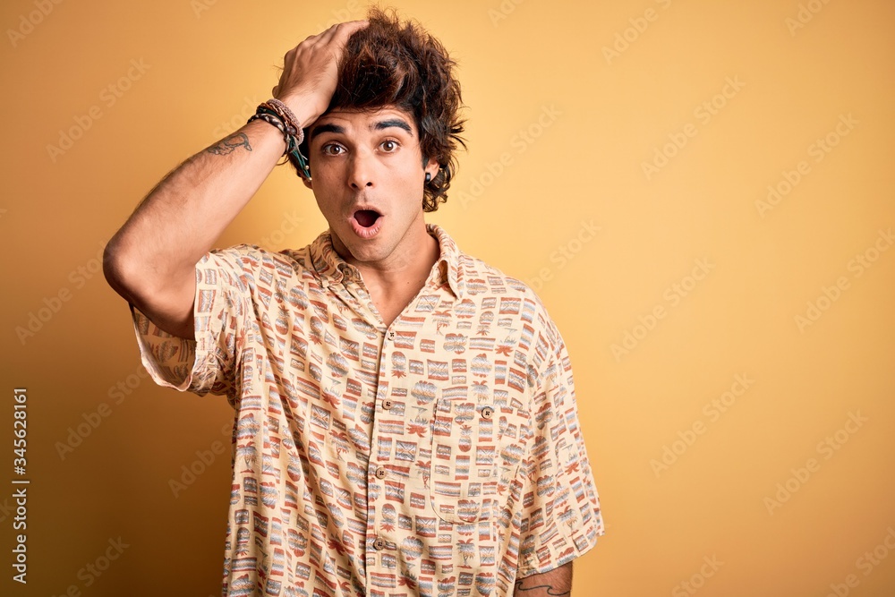 Young handsome man on vacation wearing summer shirt over isolated yellow background surprised with hand on head for mistake, remember error. Forgot, bad memory concept. Young handsome man on vacation wearing summer shirt over isolated yellow background surprised with hand on head for mistake, remember error. Forgot, bad memory concept.