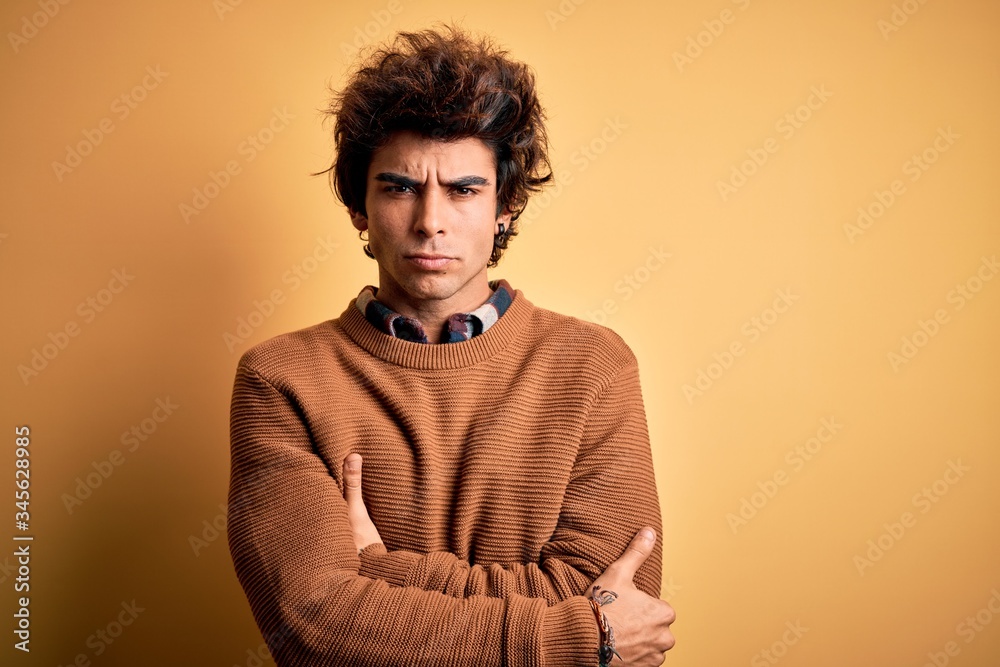 Young handsome man wearing casual shirt and sweater over isolated yellow background skeptic and nervous, disapproving expression on face with crossed arms. Negative person. Young handsome man wearing casual shirt and sweater over isolated yellow background skeptic and nervous, disapproving expression on face with crossed arms. Negative person.