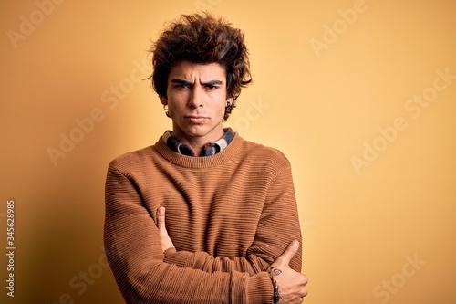 Young handsome man wearing casual shirt and sweater over isolated yellow background skeptic and nervous, disapproving expression on face with crossed arms. Negative person.