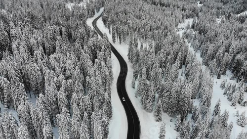 Aerial footage of car driving along curvy road in snow covered landscape