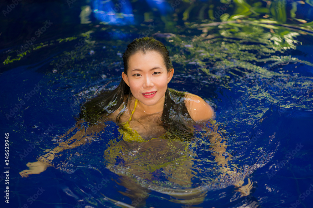 young beautiful and happy Asian Korean woman in bikini enjoying vacation at swimming pool relaxed and cheerful bathing at villa or luxury tropical resort