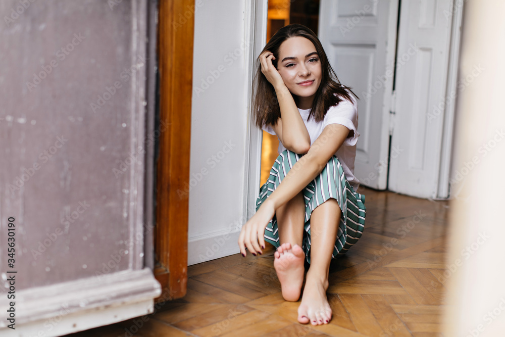 Fototapeta premium Spectacular female model in pajamas chilling at home. Indoor photo of joyful brunette girl posing on the floor.