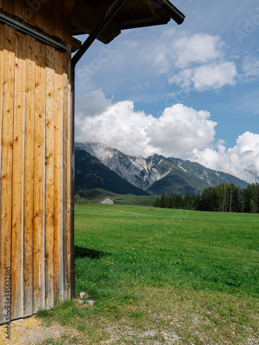 View on Tyrol mountains on a sunny day with green meadow partially covered by wooden hut.