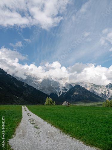 View on Tyrol mountains with green meadow and a gravelly path leading towards the mountains. With partly cloudy sky.