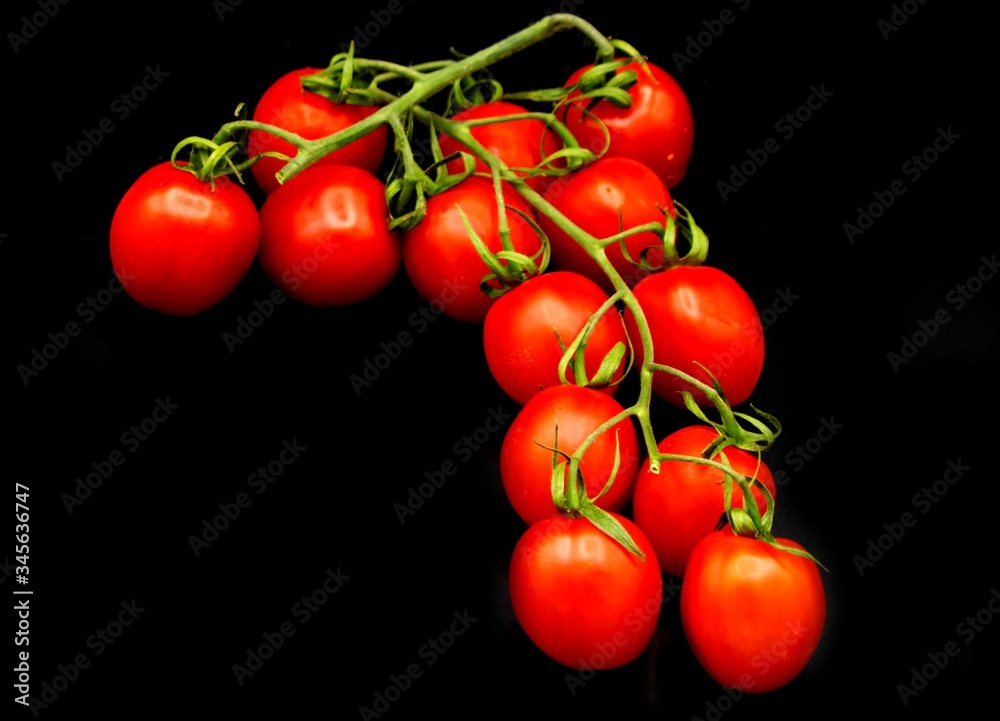 red cherry tomatoes with a green stem lie on a black background top view, isolated