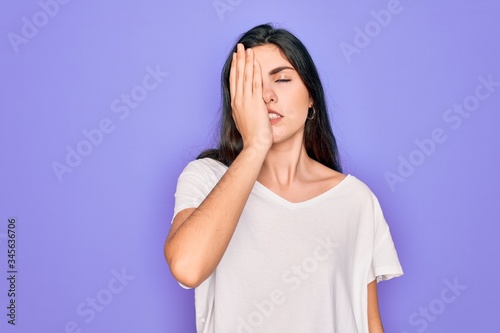 Young beautiful brunette woman wearing casual white t-shirt over purple background Yawning tired covering half face, eye and mouth with hand. Face hurts in pain. © Krakenimages.com