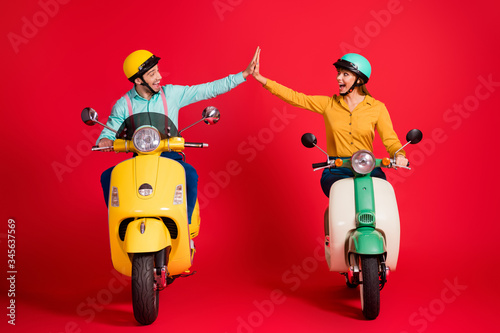 Portrait of his he her she nice attractive lovely glad lucky ecstatic cheerful cheery couple riding moped giving high five having fun isolated over bright vivid shine vibrant red color background