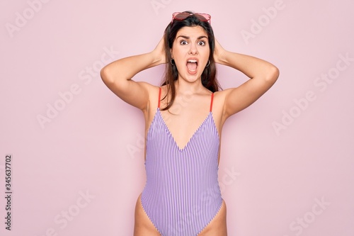 Young beautiful fashion girl wearing swimwear swimsuit and sunglasses over pink background Crazy and scared with hands on head  afraid and surprised of shock with open mouth