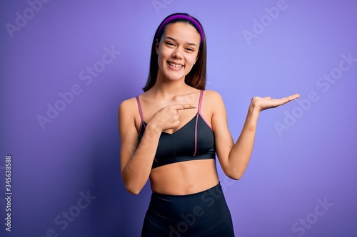Young beautiful sporty girl doing sport wearing sportswear over isolated purple background amazed and smiling to the camera while presenting with hand and pointing with finger.