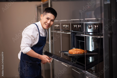 Young Adult Asian Man Baking Homemade Bakery and Taking Bread from the Oven - Cooking in the Kitchen at Home