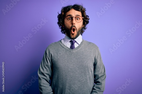 Handsome businessman with beard wearing tie and glasses standing over purple background afraid and shocked with surprise expression, fear and excited face. © Krakenimages.com