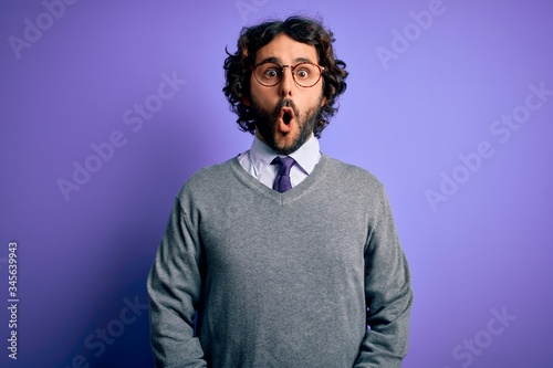 Handsome businessman with beard wearing tie and glasses standing over purple background afraid and shocked with surprise expression, fear and excited face.
