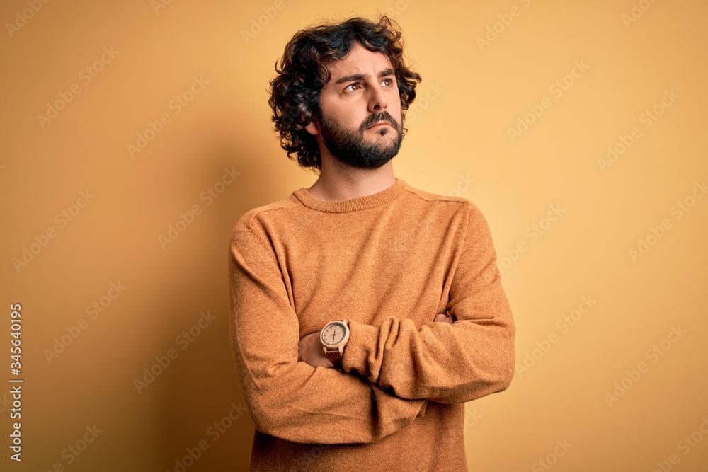 Fototapeta premium Young handsome man with beard wearing casual sweater standing over yellow background looking to the side with arms crossed convinced and confident