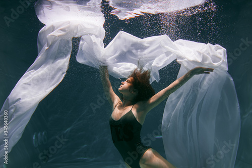 Beautiful girl swims underwater with long hair. Blue or gold background like gold. The atmosphere of a fairy tale or magic. Diving under the water with a shiny cloth