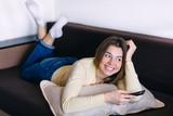 Young smiling woman watching tv while lying on a sofa at home.
