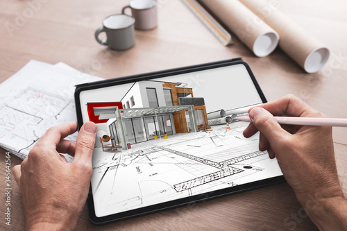 Fototapeta Naklejka Na Ścianę i Meble -  Tablette numérique tenue en main par un architecte qui travaille et réalise l'esquisse d'un projet de construction d'une maison en 3D