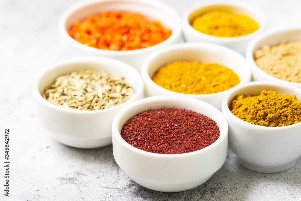 Spices and condiments in white bowls on a light gray table. Turmeric, ginger, curry, fennel and sumac in white bowls. Spices close up with space for text Spices and condiments in white bowls on a light gray table. Turmeric, ginger, curry, fennel and sumac in white bowls. Spices close up with space for text