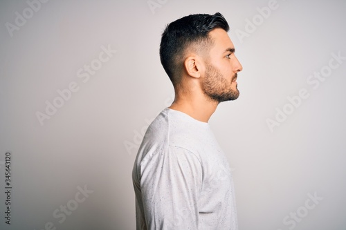 Young handsome man wearing casual t-shirt standing over isolated white background looking to side, relax profile pose with natural face with confident smile.
