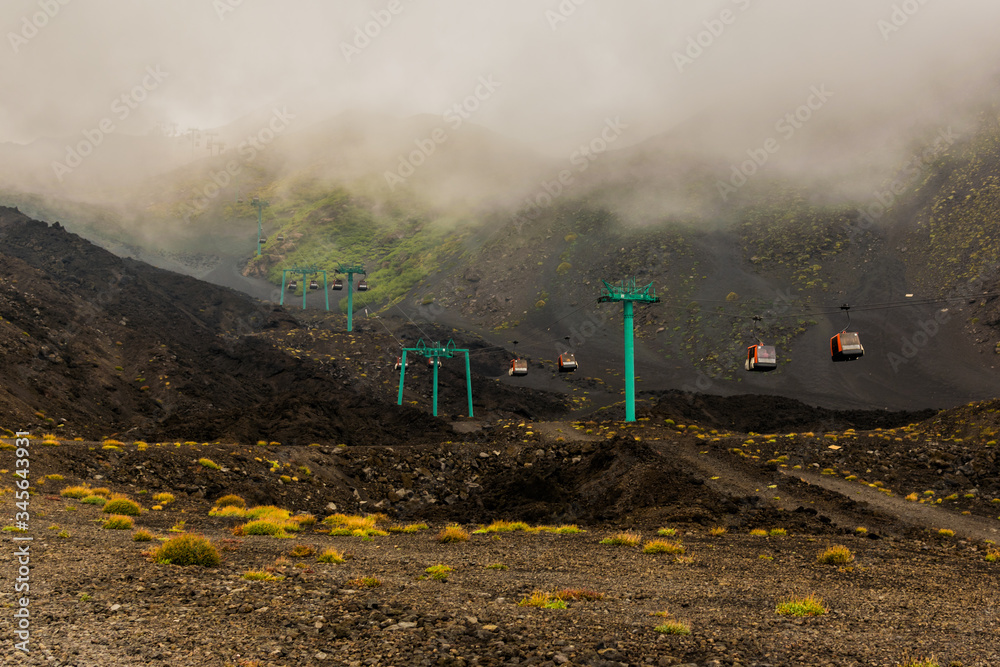 Naklejka premium Etna volcano, Sicily, Italy. Mars-like or Moon-like landscape, hiking in the clouds. In the background cable car - transport to the top of mountain. Easier way (than climbing) to get to the crater.