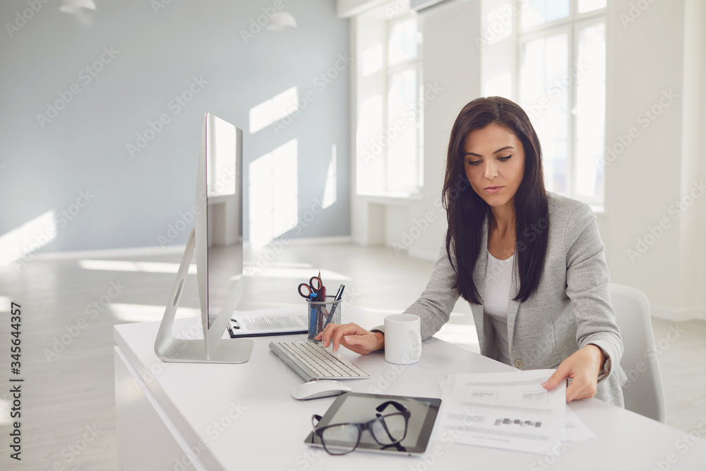 Serious busy businesswoman reads working documents sitting at a table with a computer Serious busy businesswoman reads working documents sitting at a table with a computer