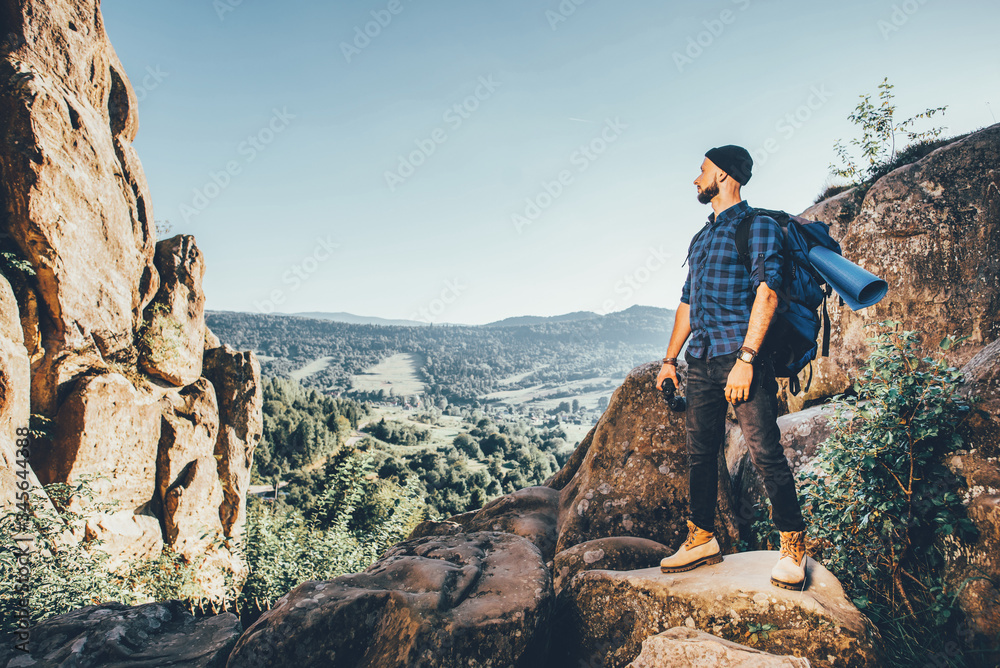 A traveler man with big backpack standing on the rocks and looking forward. Toned photo A traveler man with big backpack standing on the rocks and looking forward. Toned photo