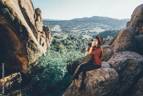 Young woman wearing hipster clothes with vintage photocamera traveling by the rocky mountains. Toned photo