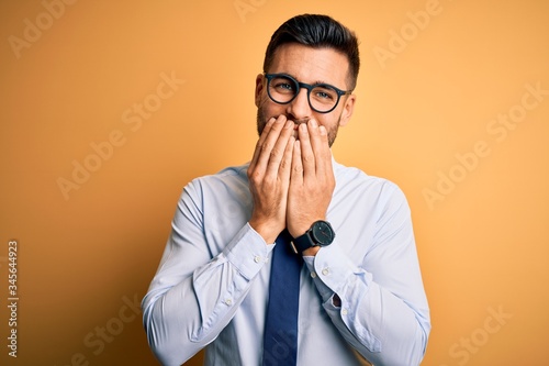 Foto Young handsome businessman wearing tie and glasses standing over yellow backgrou