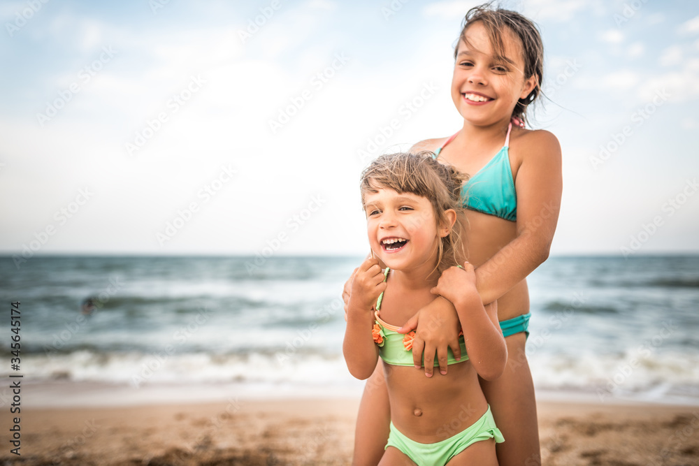 Two cute positive little girls sisters raised their hands up while swimming at sea during the holidays on a warm summer day. Concept of healthy and joyful children