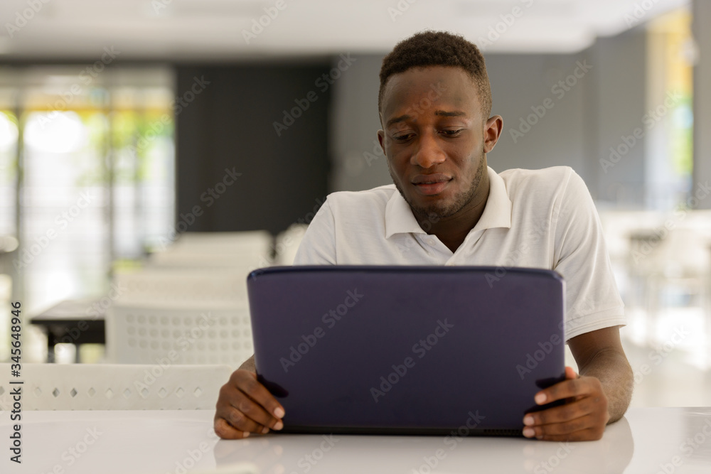 Portrait of young African man using laptop inside modern building Portrait of young African man using laptop inside modern building