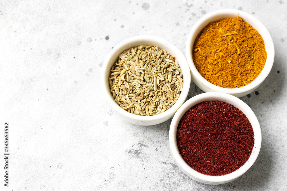 Spices and condiments in white cups on a light gray table.Fennel, sumac, curry in white bowls. Spices close up with space for text