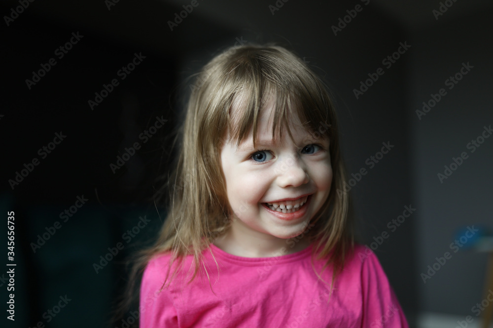 Portrait of happy child smiling and posing on camera in room. Blonde kid wearing pink tshirt and look cheerful. Childhood modeling and little beauty concept Portrait of happy child smiling and posing on camera in room. Blonde kid wearing pink tshirt and look cheerful. Childhood modeling and little beauty concept
