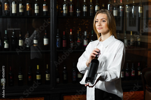 Fotografie Young pretty girl sommelier serving & presenting bottles of red and white of wine