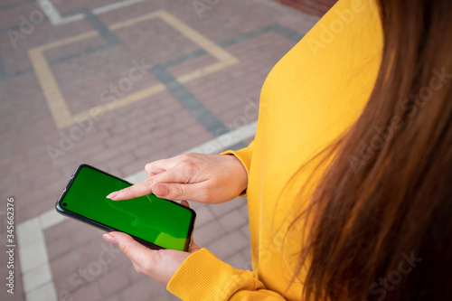 Young girl in a yellow sweater holds a phone with a green screen and scrolls photo