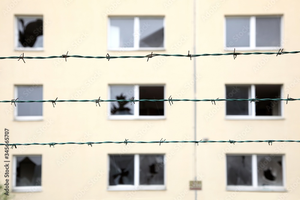 Rows of barbed wire against a abandoned residential building with broken windows background. Ghost Town, Isolation and security concept. Focus on a fence. concept of prison, salvation, Refugee, lonely
