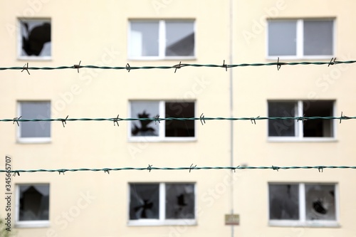 Rows of barbed wire against a abandoned residential building with broken windows background. Ghost Town, Isolation and security concept. Focus on a fence. concept of prison, salvation, Refugee, lonely