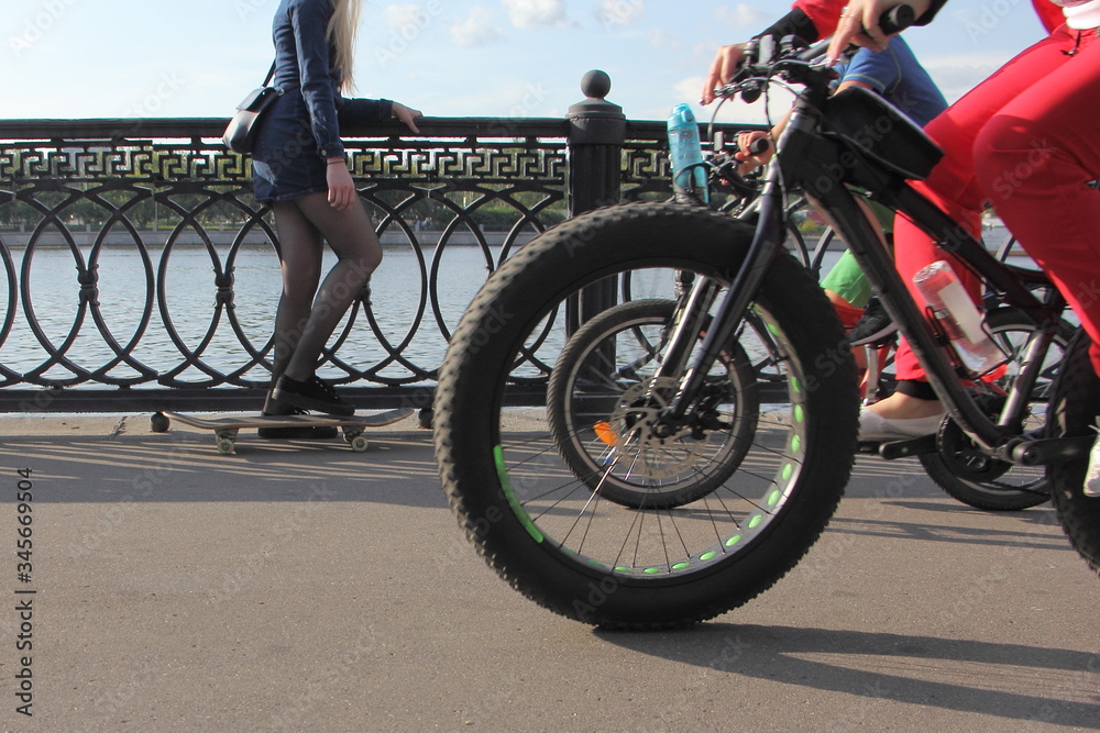 Fat bike wheel on background of skateboarder girl, summer outdoor activity sports, bicycle and skate board in Moscow Park