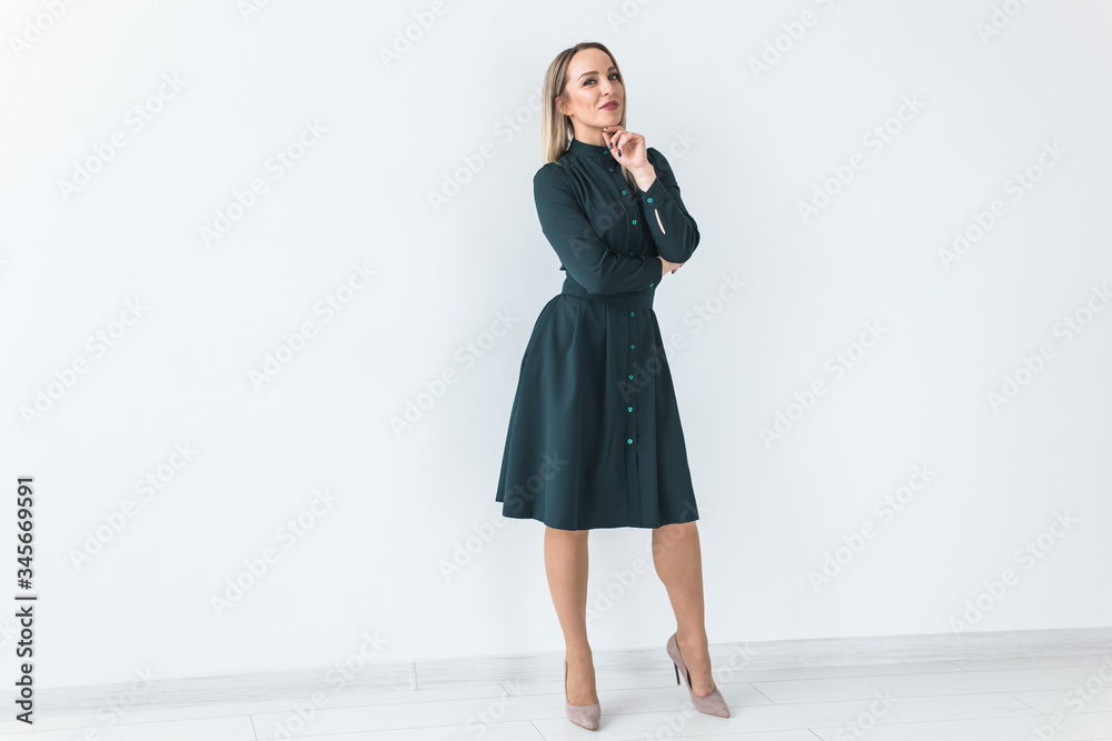 Fashionable young blonde woman in beautiful elegant dress posing at white studio with copy space. Fashionable young blonde woman in beautiful elegant dress posing at white studio with copy space.