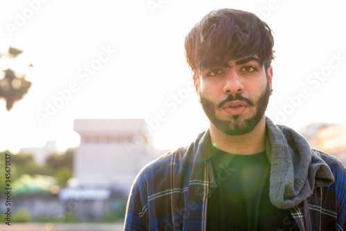 Young handsome bearded Indian hipster man in urban streets