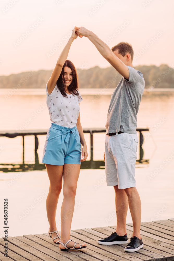 Loving young couple dancing on pier at sunset in summer.