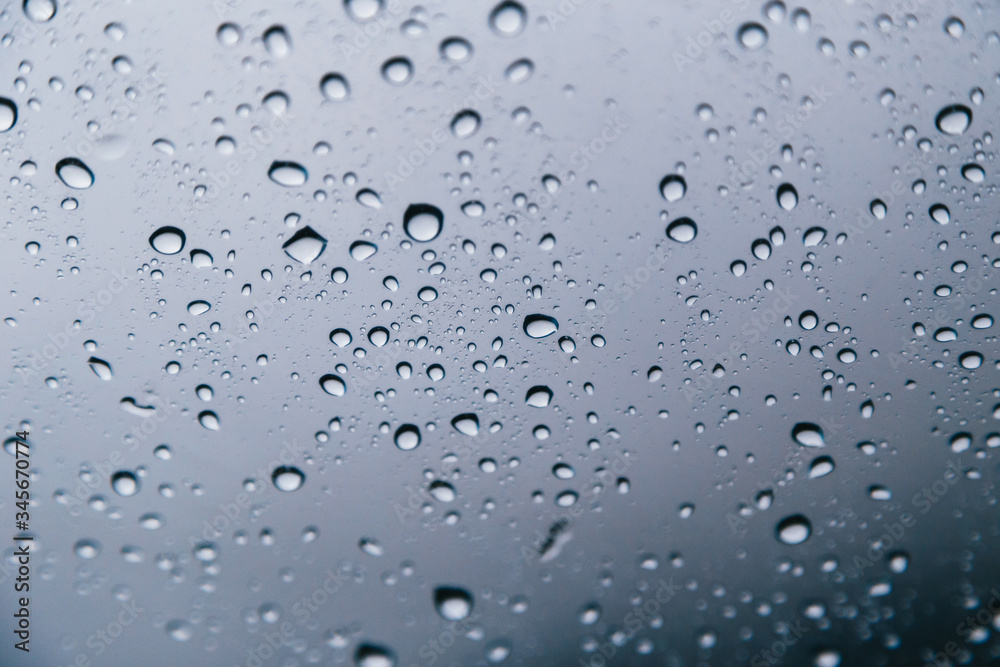 Close up of rain drops on the windshield, front window of a car on a blue gray background of dark sky. Close up of rain drops on the windshield, front window of a car on a blue gray background of dark sky.
