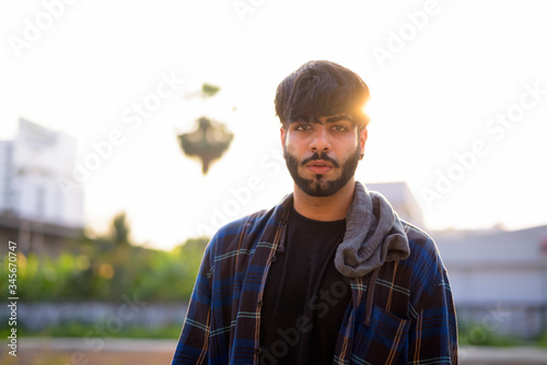 Young handsome bearded Indian hipster man in urban streets