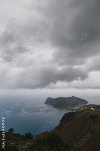 A top view at Asos village and Assos peninsula from a road during the bad weather conditions, thunderstorm and rain, with low dark clouds and visible currents at sea. Cephalonia, Greece.