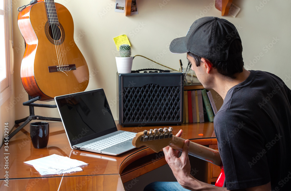 Young man in cap playing and learning electric guitar using a laptop at  home. Musician playing guitar in his room. Concept of learn guitar online.  Stock Photo | Adobe Stock