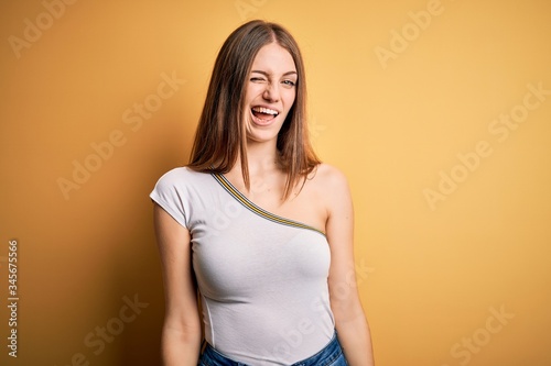 Young beautiful redhead woman wearing casual t-shirt over isolated yellow background winking looking at the camera with sexy expression, cheerful and happy face. © Krakenimages.com