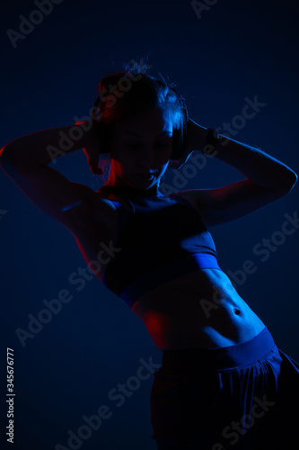 Curved female figure with neon straight muscles of the press. Athletic girl presses headphones in her head.