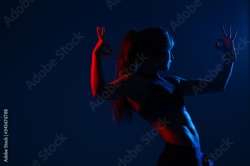 Fototapeta Naklejka Na Ścianę i Meble -  A sports girl with embossed oblique backlit muscles of the press shows a sign of approx. The hand is highlighted in red.