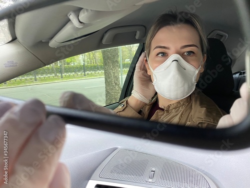 girl in a protective mask looks in the mirror in a car. During quarantine- coronavirus.  Covid-19.